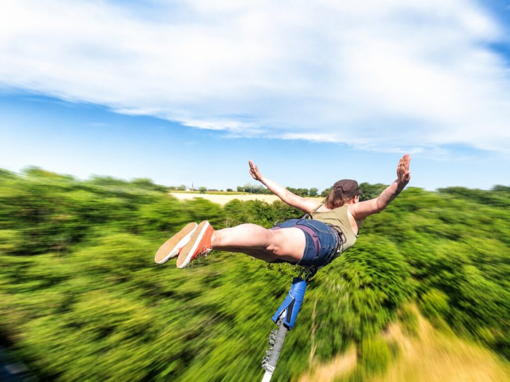 Participante réalisant un saut à l’élastique depuis un pont au cœur d’un paysage naturel.